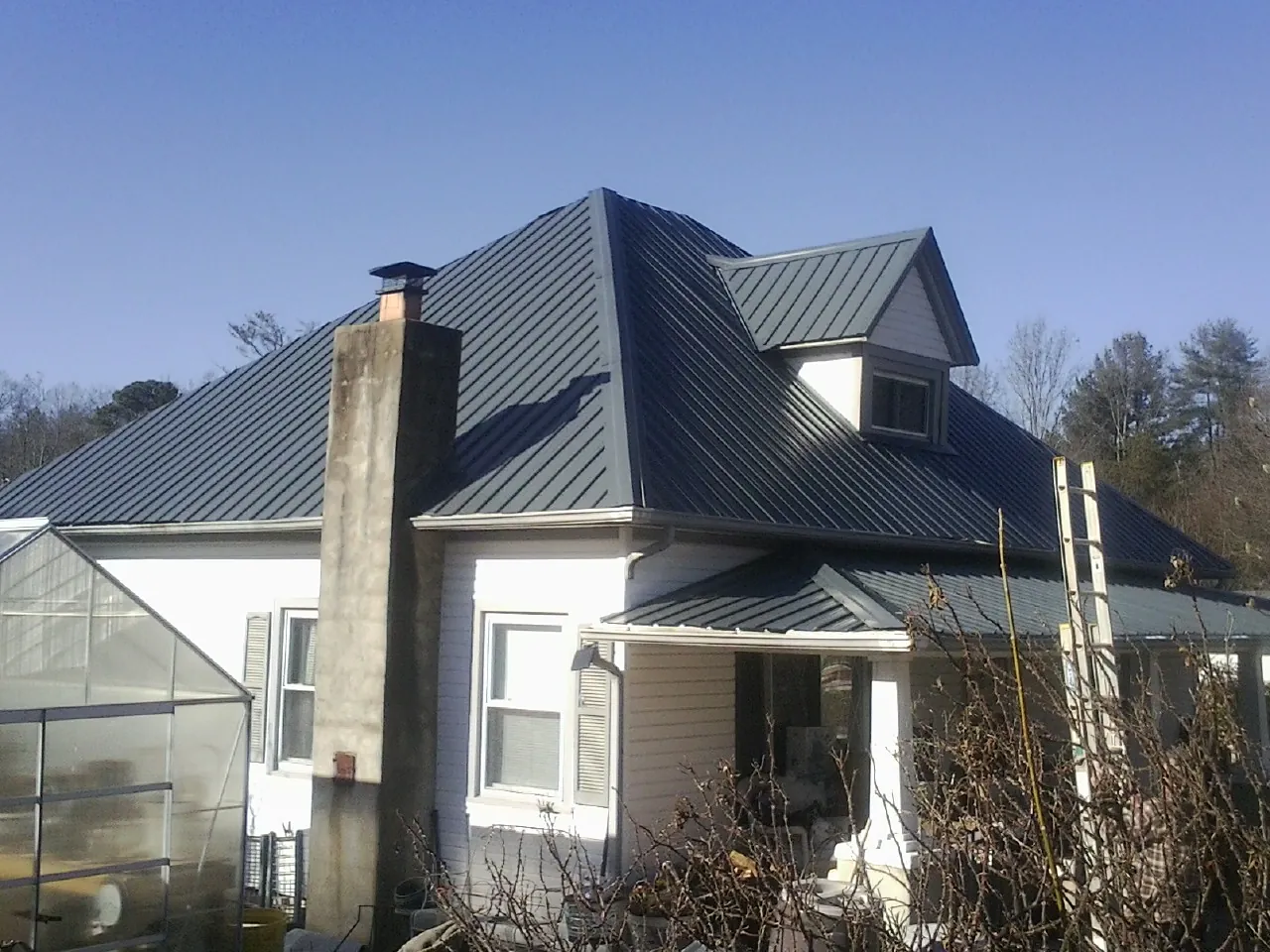 Dark blue standing seam metal roof on a white farmhouse with dormer — Slate & Tile Roof Repair by Roofing Brothers in Neversink