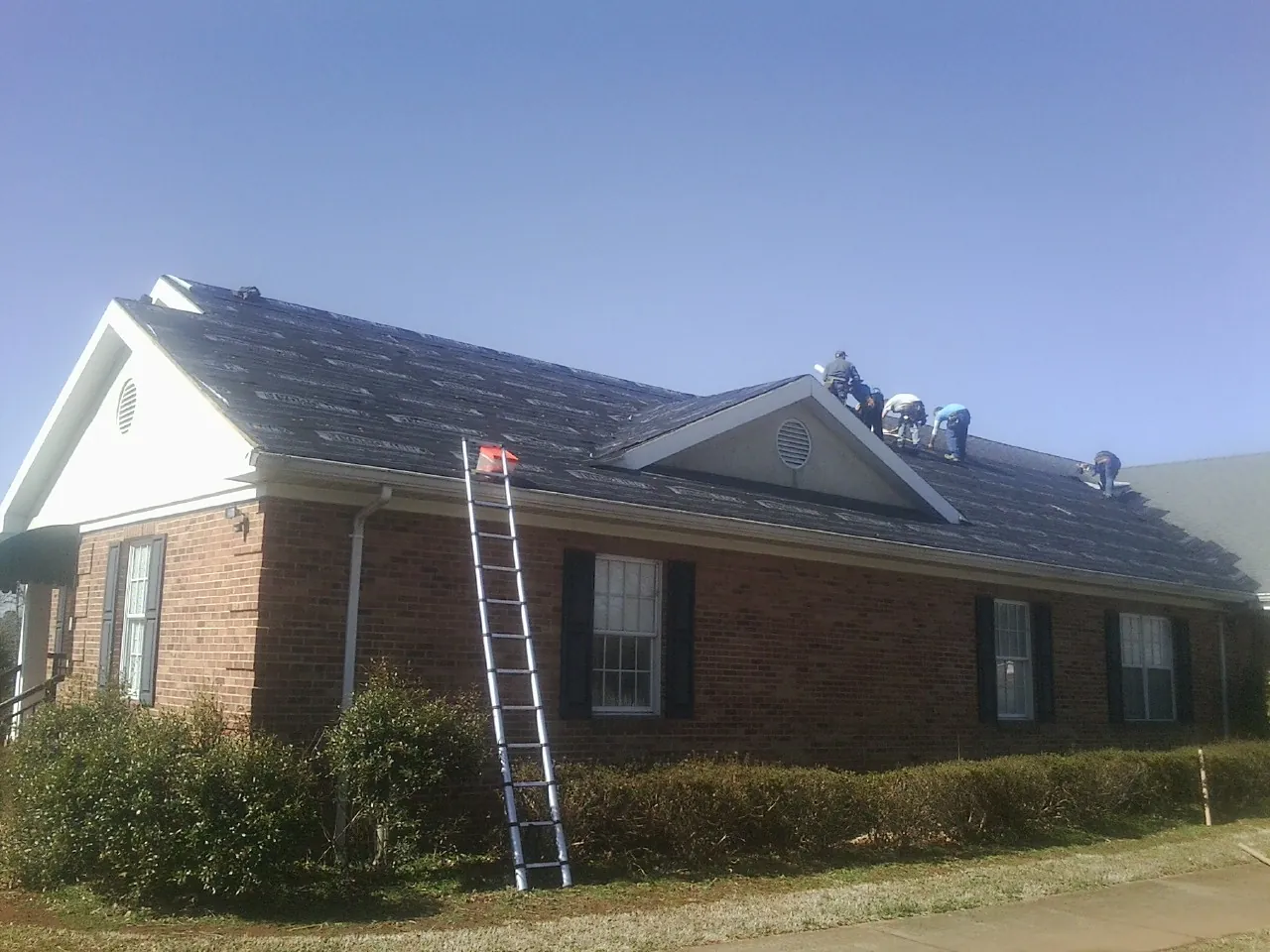 Crew tearing shingles off a brick ranch roof with a ladder set — Emergency Roof Repair work by our crew in Neversink