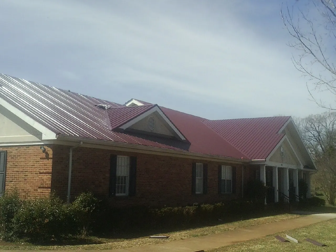 Red metal roof with gabled entries on a long brick building, from a Hail Damage Roof Repair job in Neversink