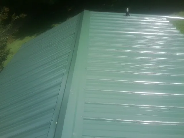 New green metal panels meeting at the ridge of a roof — Flat Roof Repair work by our crew in Neversink
