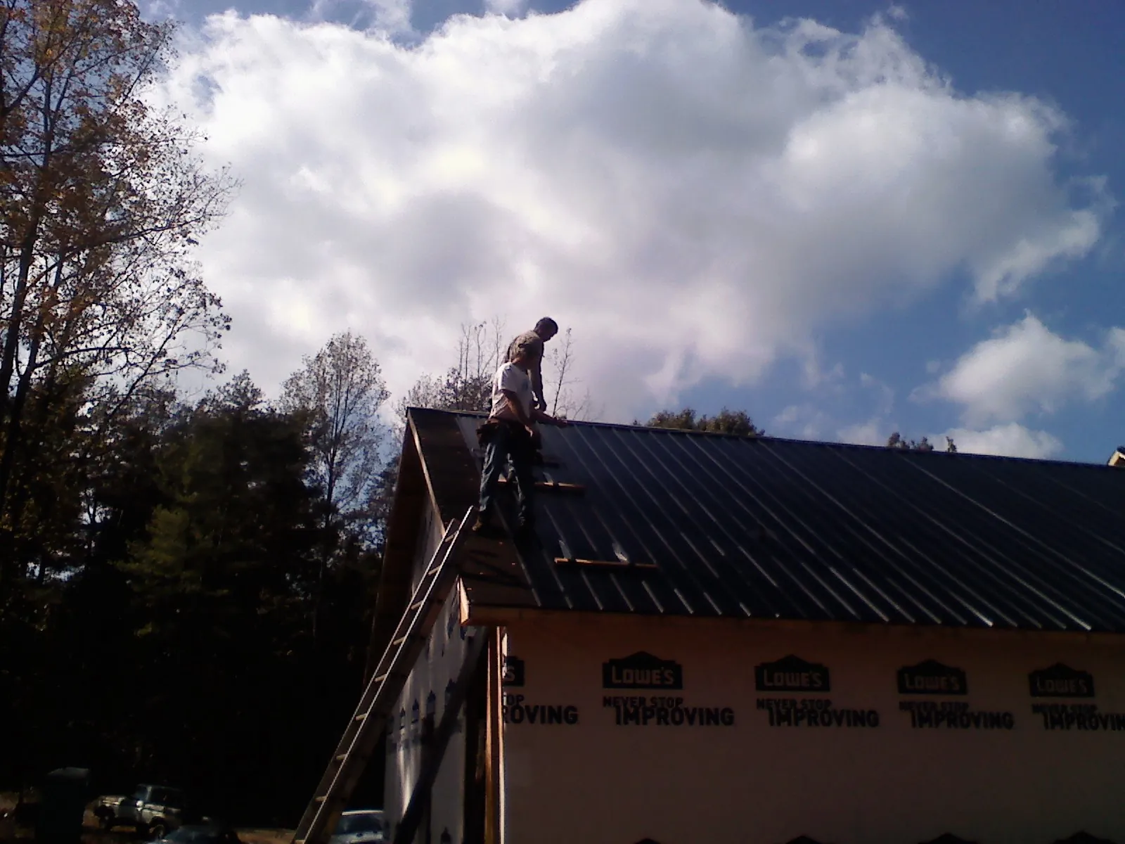 Roofer fastening dark metal panels high against a cloudy sky, from a Roof Inspection job in Neversink