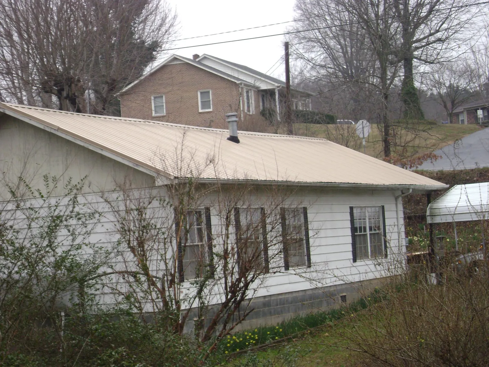 Tan metal roof on a white sided house set into a hillside — Commercial Roofing by Roofing Brothers in Neversink